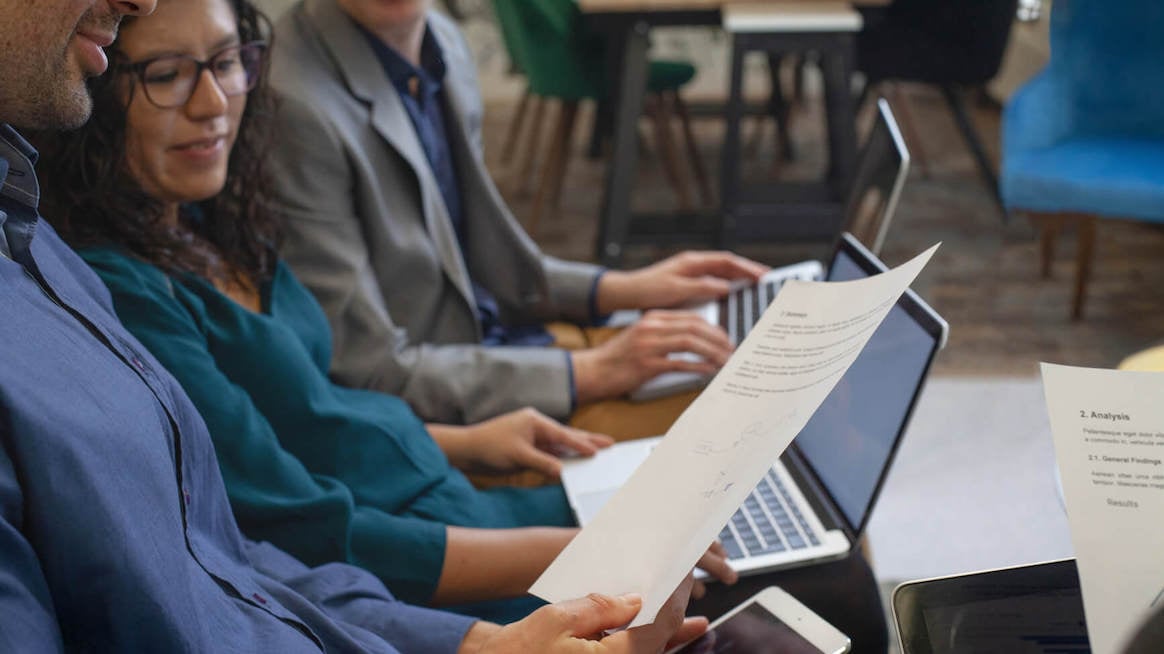people looking at laptop and piece of paper 