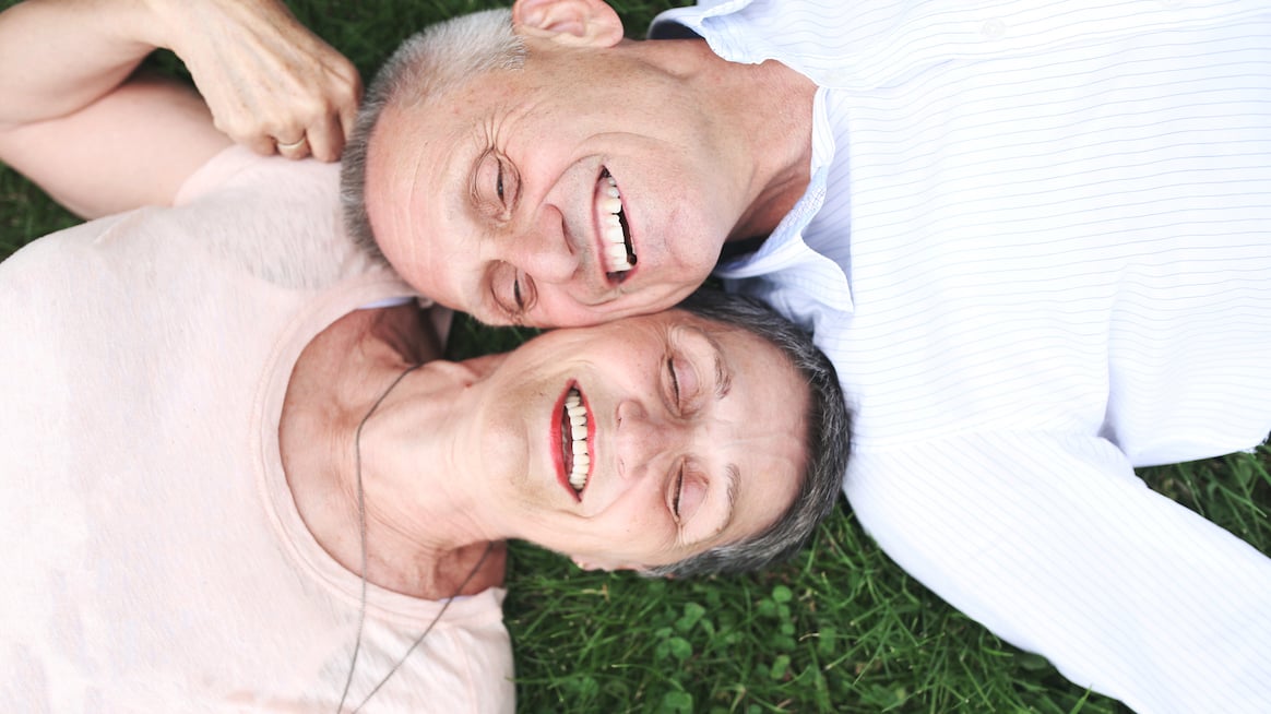two-older-people-recline-on-grass-laughing-resilience-optimism-increase-with-age