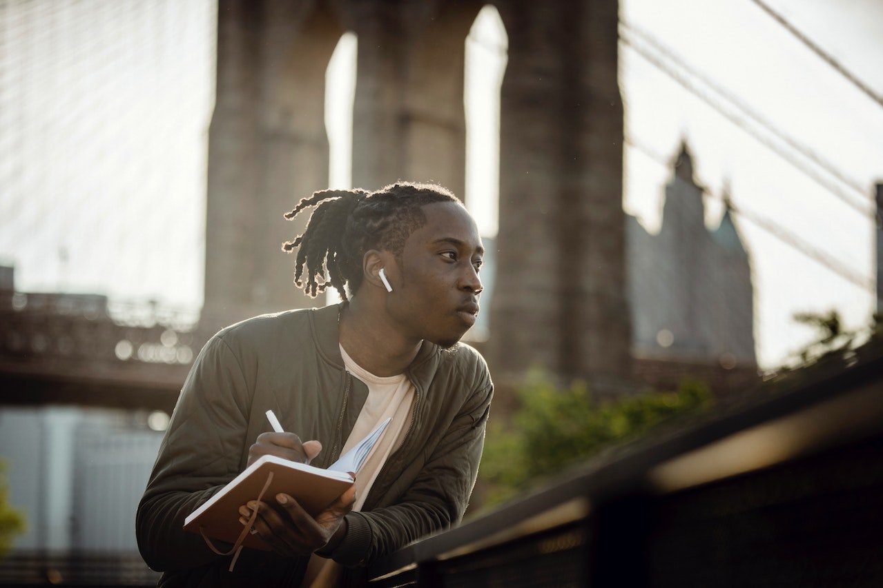 Thoughtful-man-outdoors-with-earphones-and-a-notebook-writing-down-things-to-manifest