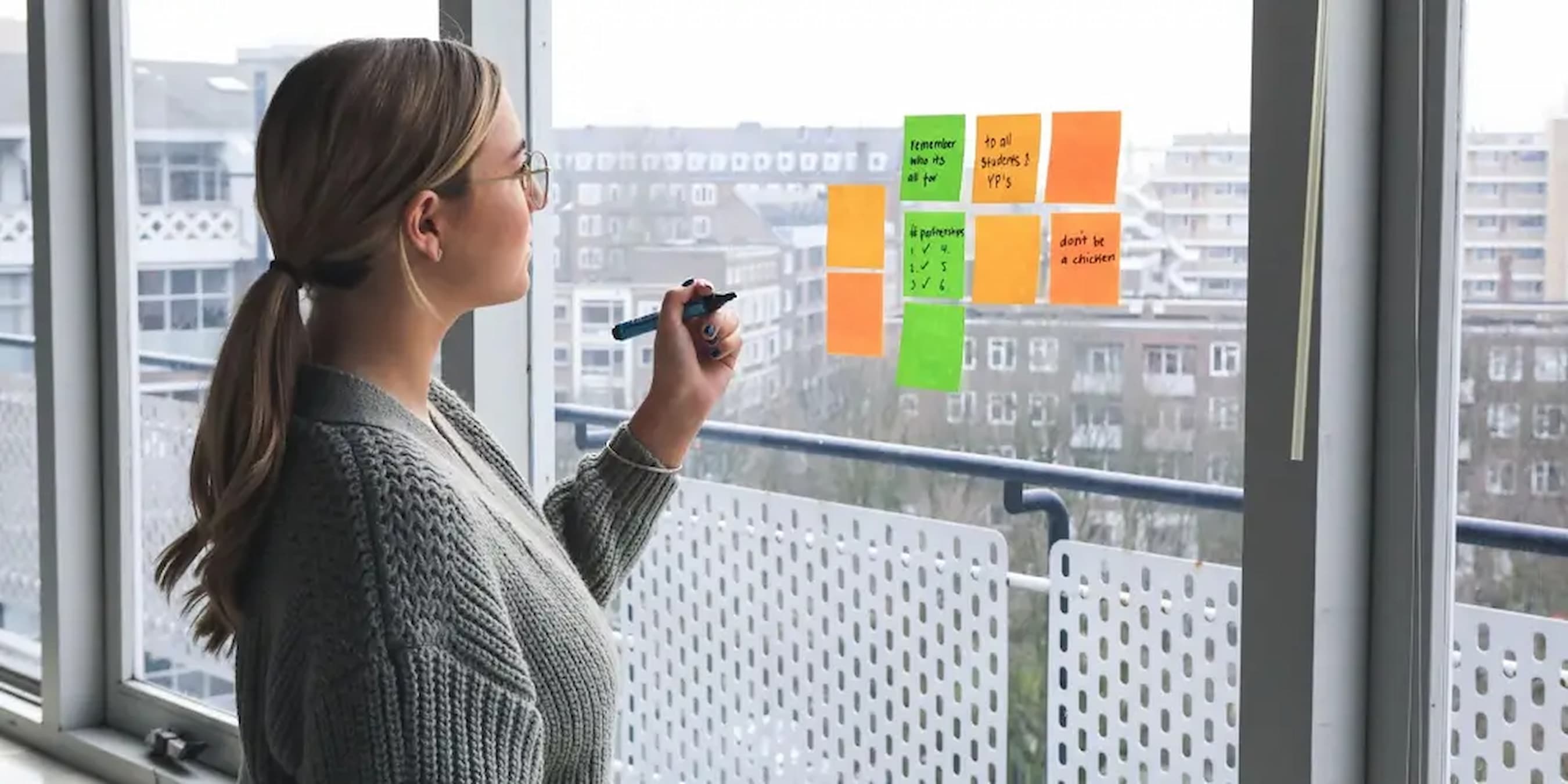 Woman-writing-on-sticky-notes-on-window-setting-goals-for-success